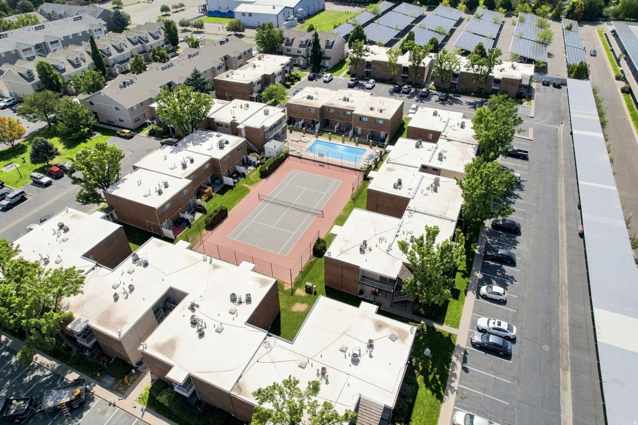 Community with multiple residential buildings, central tennis court, swimming pool, and dedicated parking areas