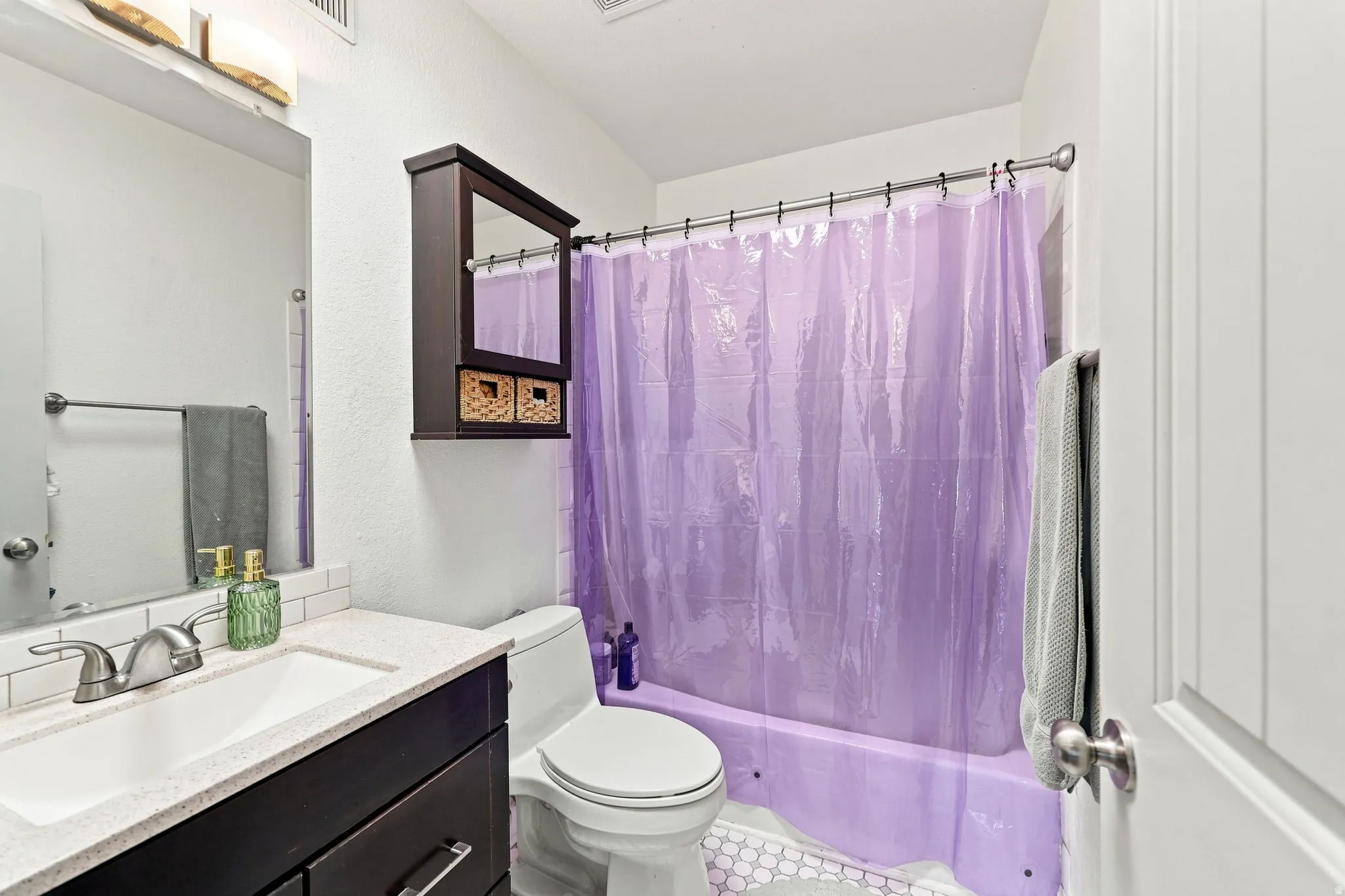 White subway tile backsplash, dark wood-finish vanity, light-toned countertop, wall-mounted mirror, and a built-in shower/tub combination