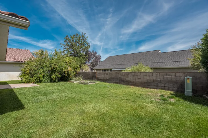 Grassed yard area, concrete paver patio, block retaining wall, mature perimeter landscaping, and shingle roof