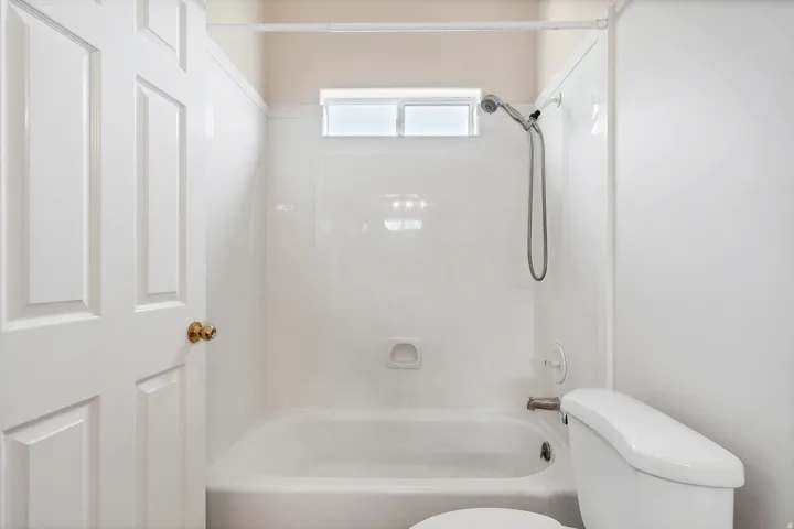 White panel door with brass hardware, tub/shower combination, white toilet, and transom window