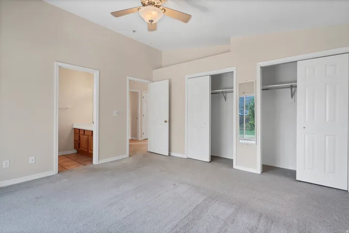 Vaulted ceiling, two sliding-door closets, ceiling fan with light fixture, light-toned carpeting, and a built-in vanity with wood cabinetry