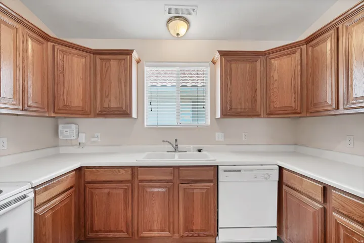 U-shaped kitchen layout featuring extensive wood cabinetry, white countertops, a double basin sink with a single-handle faucet, and a built-in dishwasher