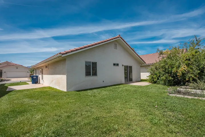 Stucco exterior with a tile roof, featuring a concrete patio and a grassy yard