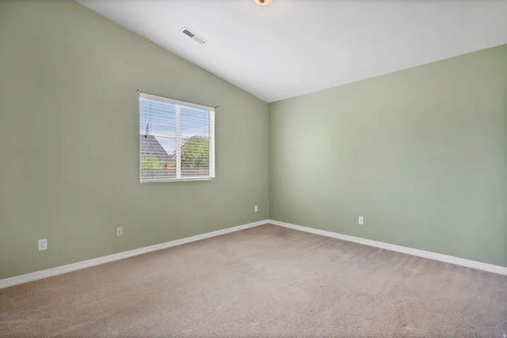 Carpeted room with vaulted ceiling and a window featuring horizontal blinds