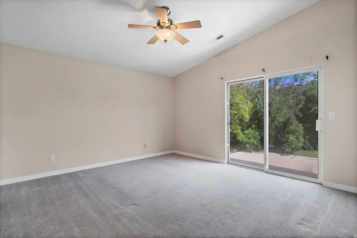 Vaulted ceiling, ceiling fan with integrated lighting, neutral wall paint, gray carpeting, and sliding glass doors with direct outdoor access