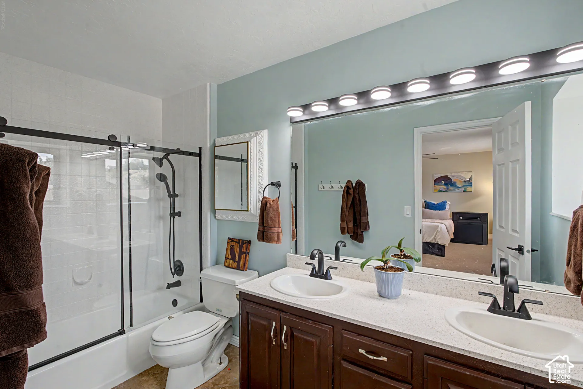 Master bathroom featuring dual vanities with frameless glass-enclosed tub/shower, new fixtures, and vanity lighting.