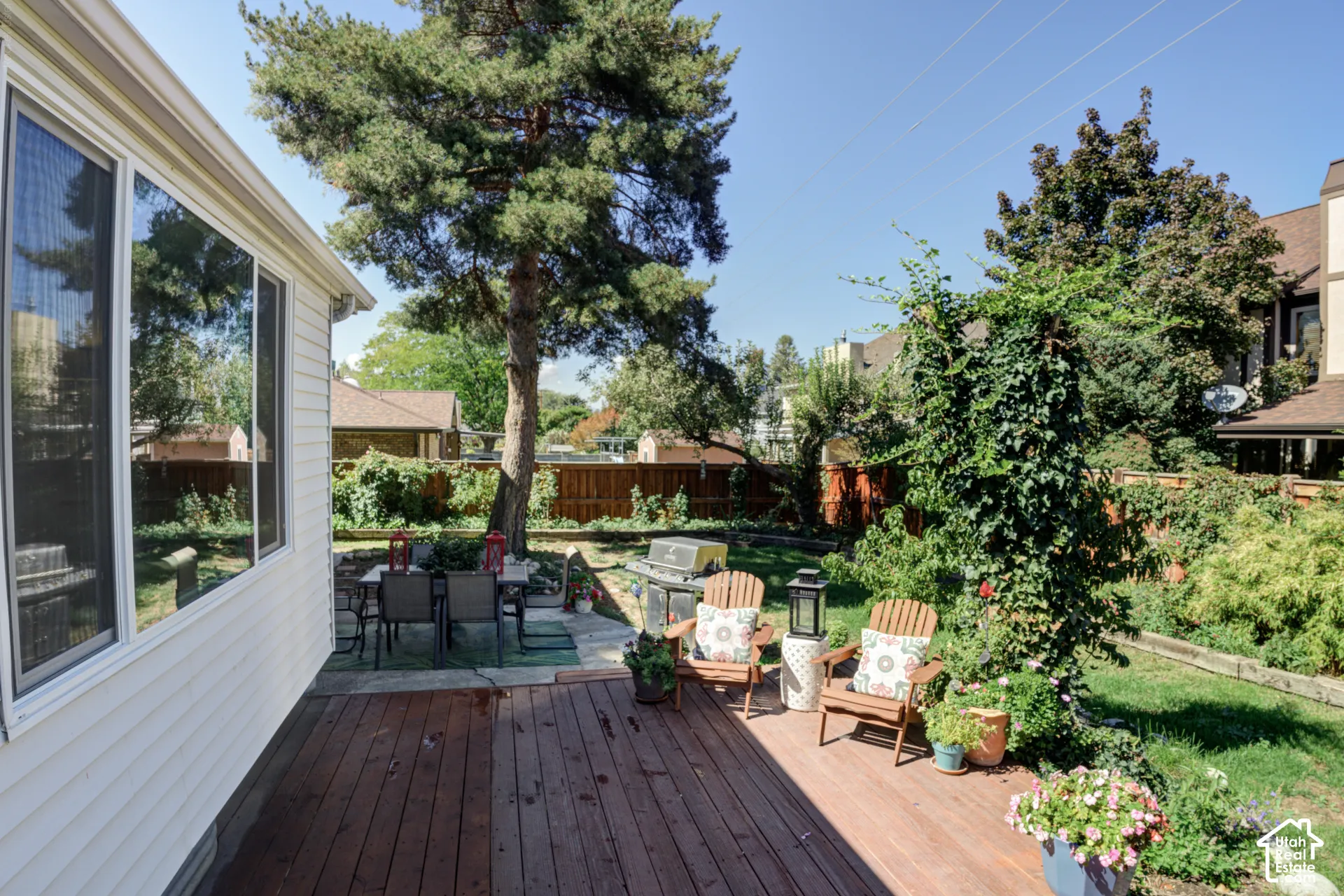 Wood-finish deck with a stone patio area, mature trees, and privacy fencing