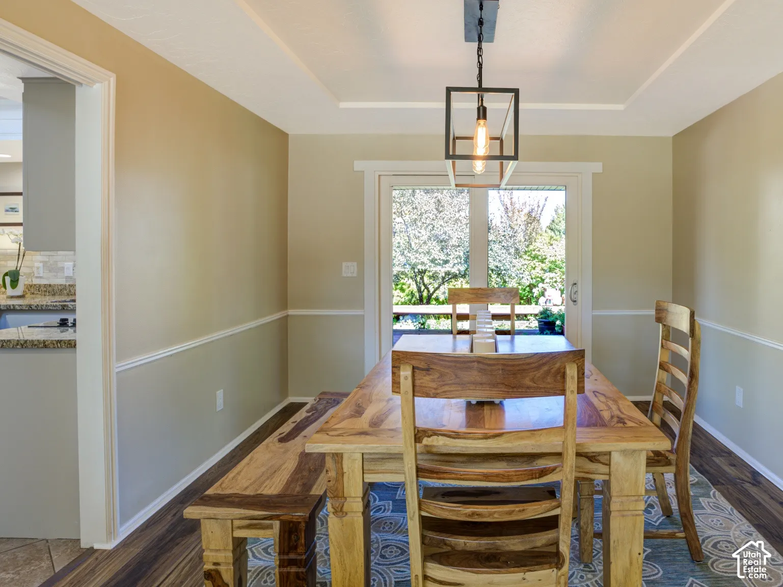 Wood-finish flooring, tray ceiling, contemporary linear light fixture, chair rail molding, and a patio door with exterior access