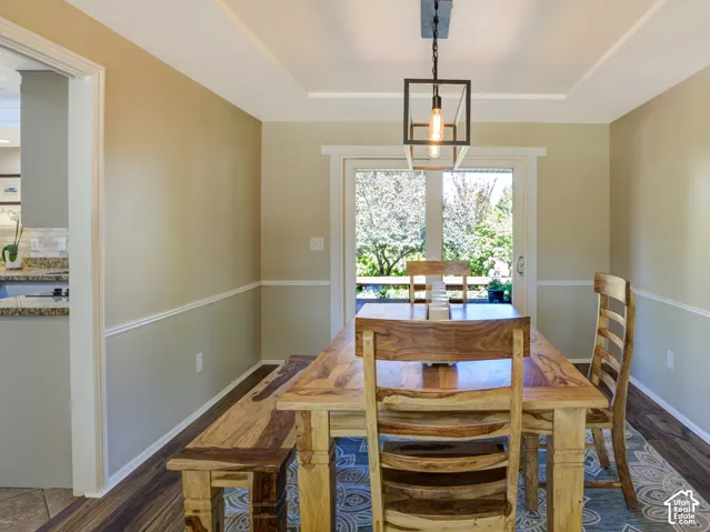 Wood-finish flooring, tray ceiling, contemporary linear light fixture, chair rail molding, and a patio door with exterior access