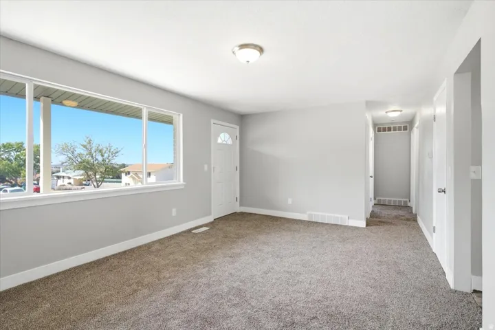 Spacious living area featuring neutral carpeting, a large picture window, and a paneled entry door with an arched glass insert
