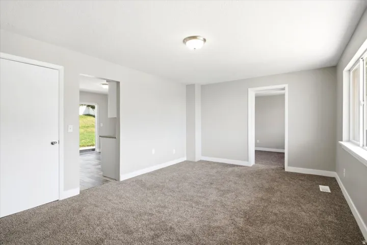 Neutral gray wall paint, brown carpet flooring, flush mount ceiling light, white window trim, and white baseboards