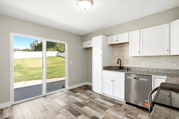 Wood-finish flooring, white cabinetry with silver hardware, stone countertops, subway tile backsplash, and a sliding glass door