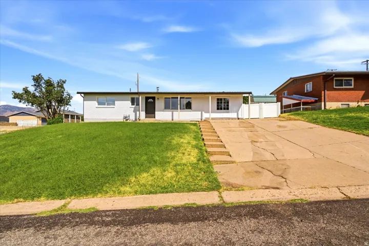 White exterior with an integrated covered porch, expansive front lawn, and a multi-step walkway