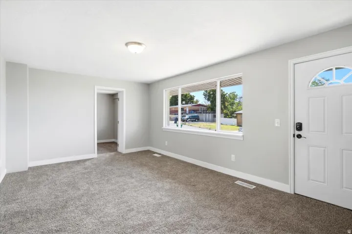 Neutral wall color, gray carpet, wide window, overhead light fixture, and a white paneled door with an arched glass insert