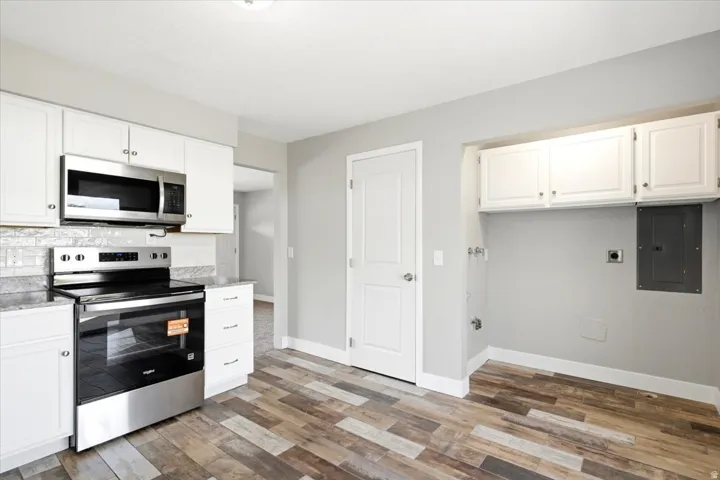 Modern kitchen featuring stainless steel appliances, white cabinetry with hardware accents, subway tile backsplash, and wood-finish flooring throughout