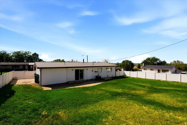 Expansive green lawn, white vinyl fencing, sliding glass door, concrete patio, and a metal roof