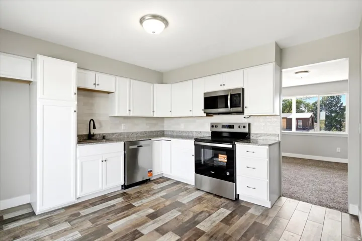 Kitchen featuring white cabinetry, stainless steel appliances, granite countertops, tile backsplash, and wood-finish flooring