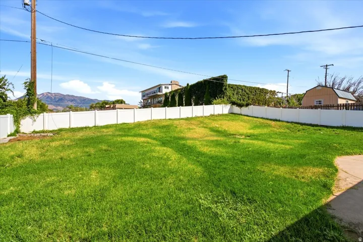 Expansive grassy lot featuring a white privacy fence and a mountain backdrop
