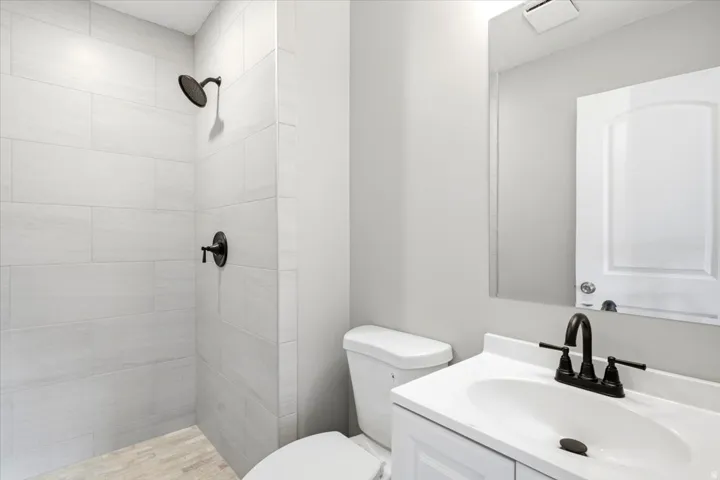Walk-in shower with light-toned rectangular wall tiles, oil-rubbed bronze shower fixtures, white vanity with integrated sink, and wall-mounted mirror