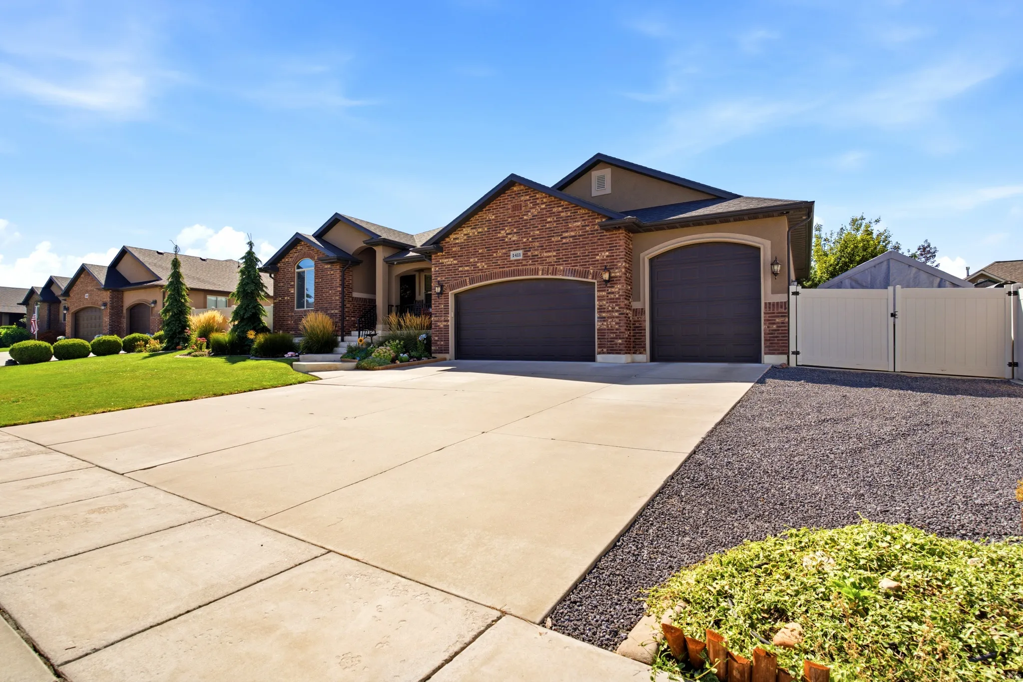 Brick and stucco exterior with arched garage doors, concrete driveway, and established front landscaping