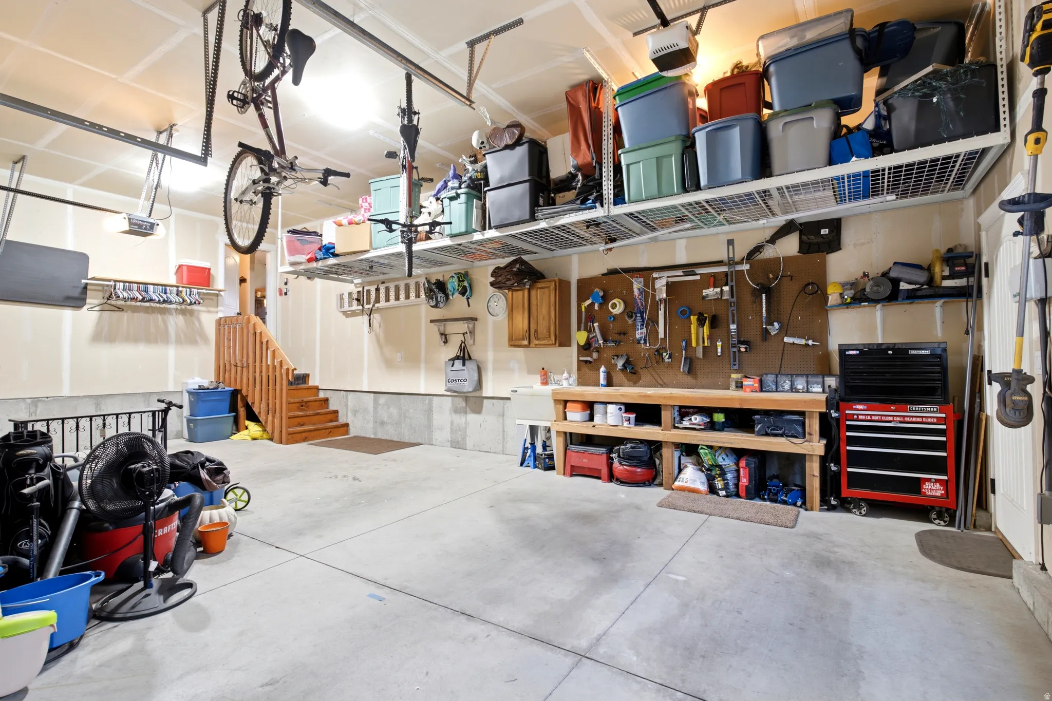 Concrete flooring with wall-mounted storage racks, a built-in workbench, and a wooden staircase