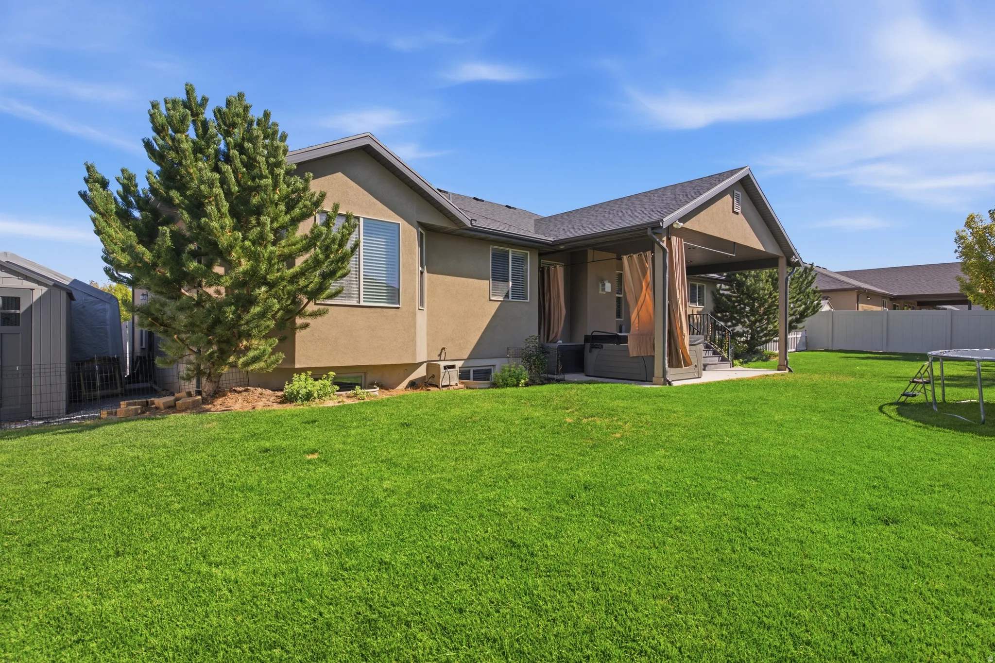 Expansive green lawn with a mature tree, an attached covered patio, and an accessory storage shed