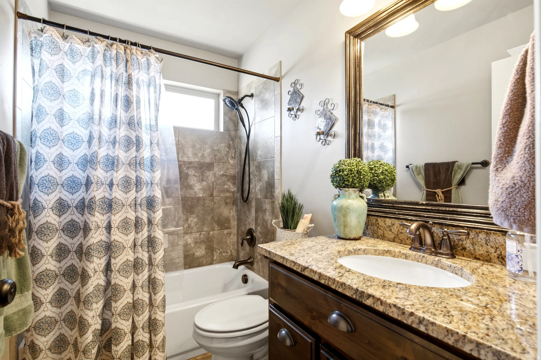 Granite-finish vanity with an oval sink, wood-finish cabinetry, and a framed mirror