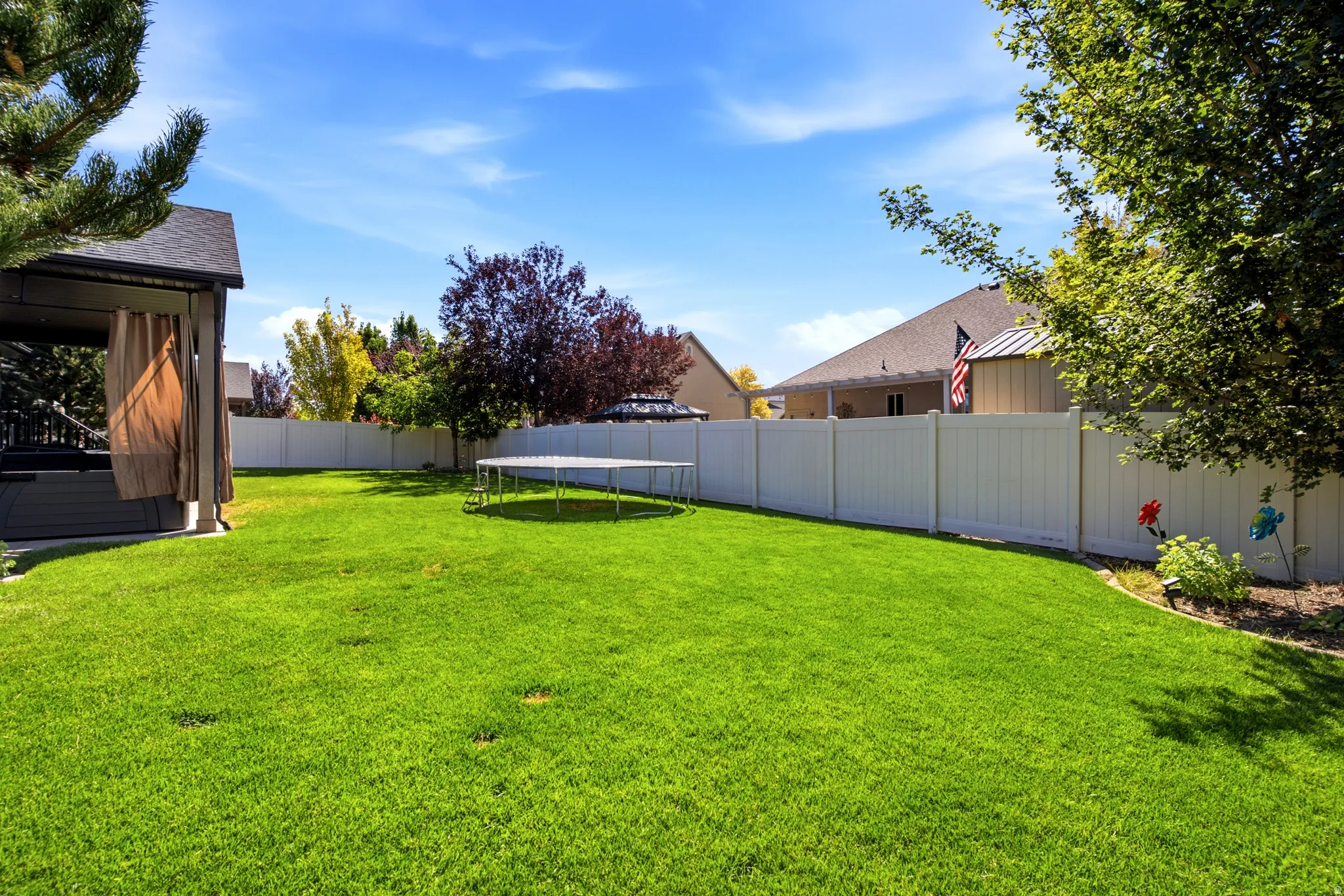 Expansive lawn area with a privacy fence, mature trees, and a covered patio structure