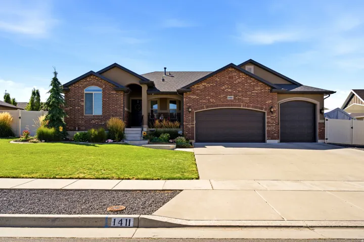 Brick and stucco exterior, arched garage doors, concrete driveway, mature landscaping, and a manicured lawn