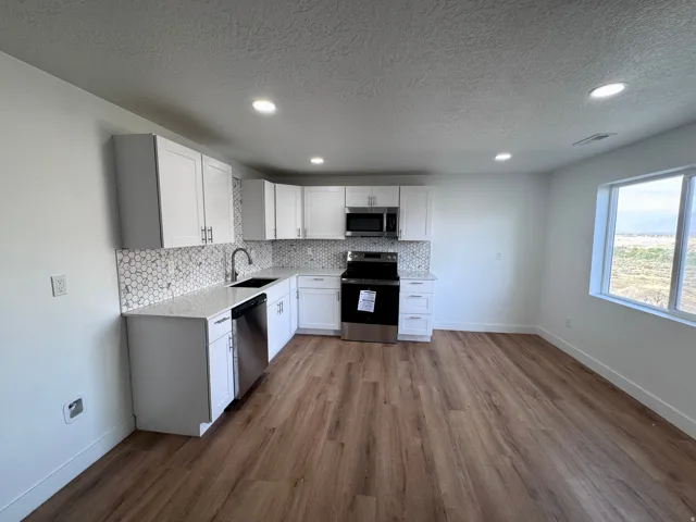 White shaker cabinetry, honeycomb tile backsplash, stainless steel appliances, wood-finish flooring, and recessed ceiling lighting
