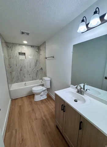 Bathroom featuring a wood-finish floor, a vanity with a single basin sink and a light-colored countertop, and a tiled shower-tub combination with a built-in niche