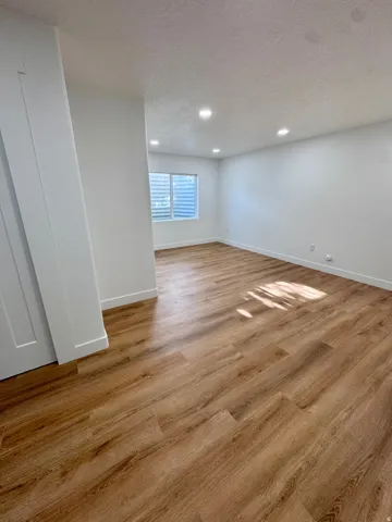Recessed lighting, wood-finish flooring, white walls, and a window with horizontal blinds