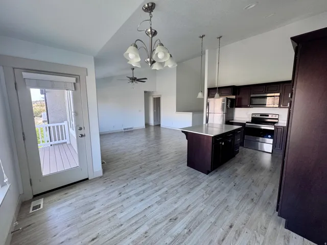 Light wood-finish flooring throughout, kitchen with dark wood cabinetry and stainless steel appliances, central island with light countertop, and a walk-out balcony