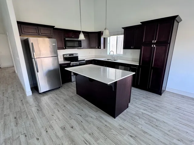 Kitchen featuring dark wood-finish cabinetry, stainless steel appliances, a center island with a light-colored countertop, and wood-finish flooring