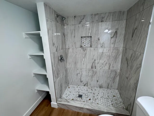 Tiled shower enclosure featuring a built-in niche, chrome fixtures, and a hexagonal tile floor