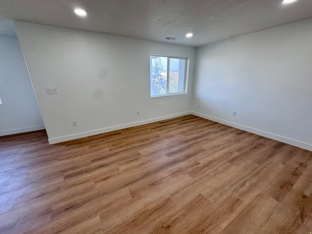 Recessed lighting illuminates the wood-finish flooring and white walls