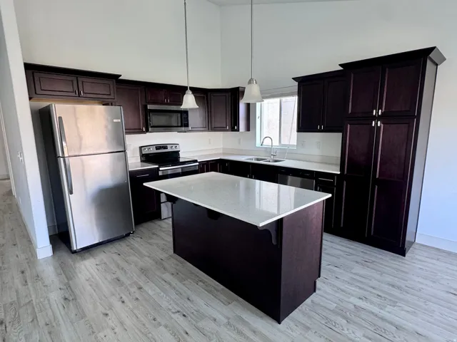 Kitchen featuring a center island with solid surface countertop, wood-finish flooring, dark wood cabinetry, and stainless steel appliances