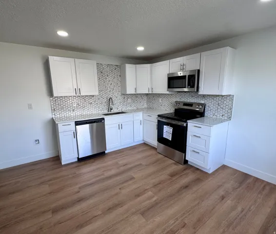 White shaker cabinetry with stainless steel hardware, quartz countertops, full-height hexagonal tile backsplash, stainless steel appliances, and wood-finish flooring