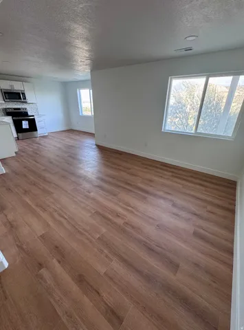 Wood-finish flooring, white walls, recessed ceiling lighting, kitchen cabinetry, and stainless-steel appliances
