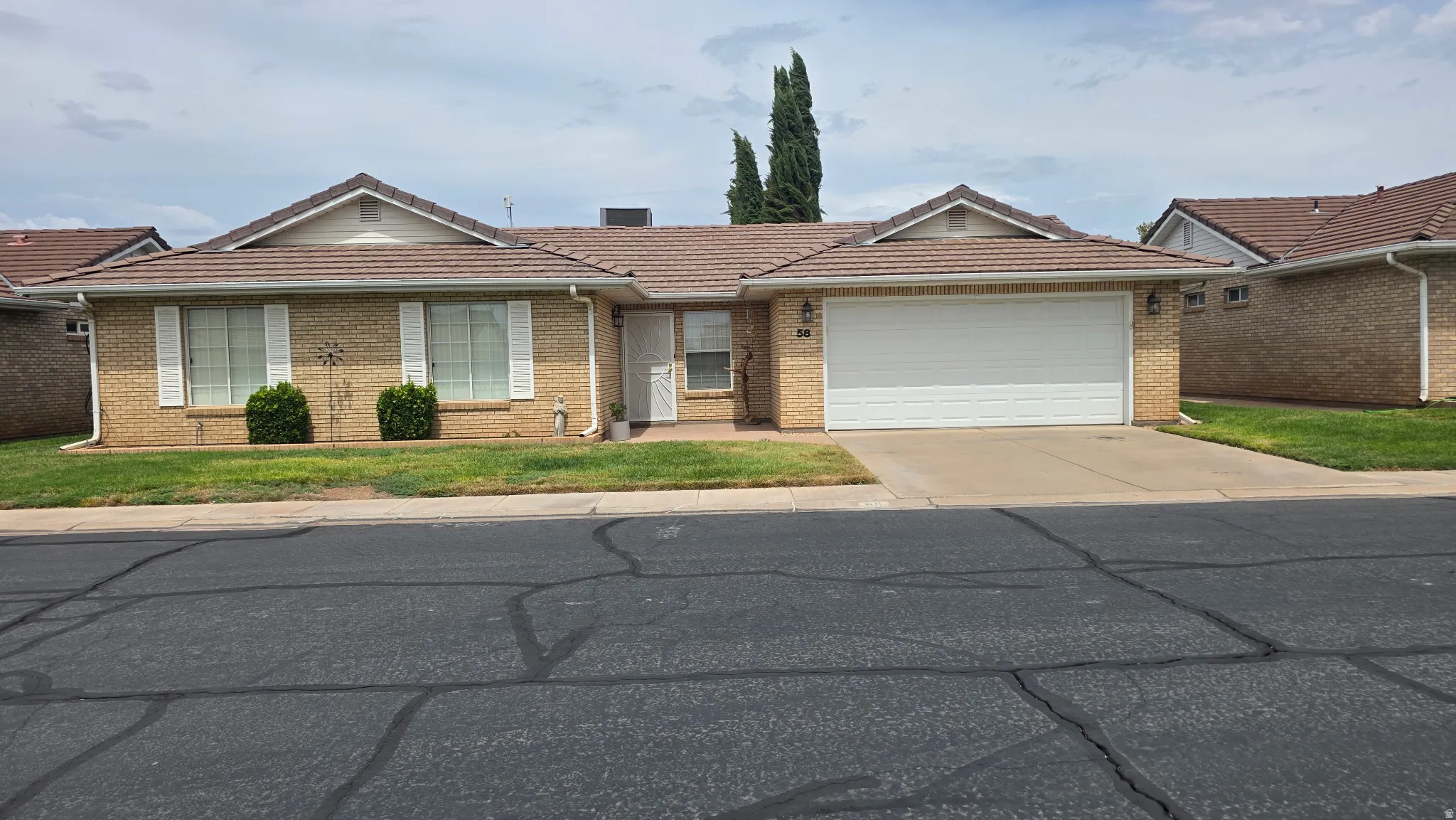 Brick exterior with a tiled roof, attached two-car garage, and white window shutters
