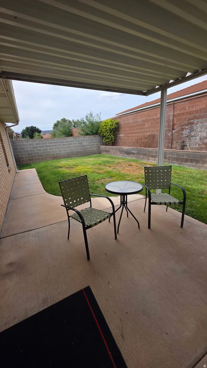 Covered patio with a concrete slab, leading to a grass area bordered by a block wall