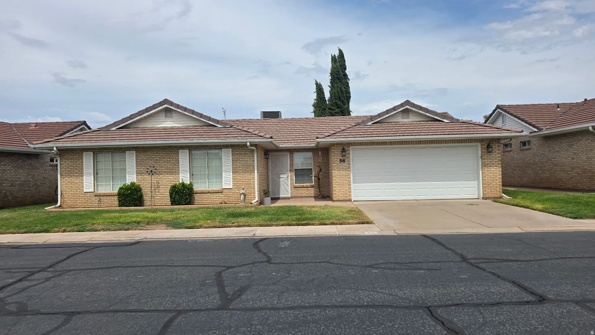 Brick exterior, tile roof, attached garage, well-maintained landscaping, and white window shutters