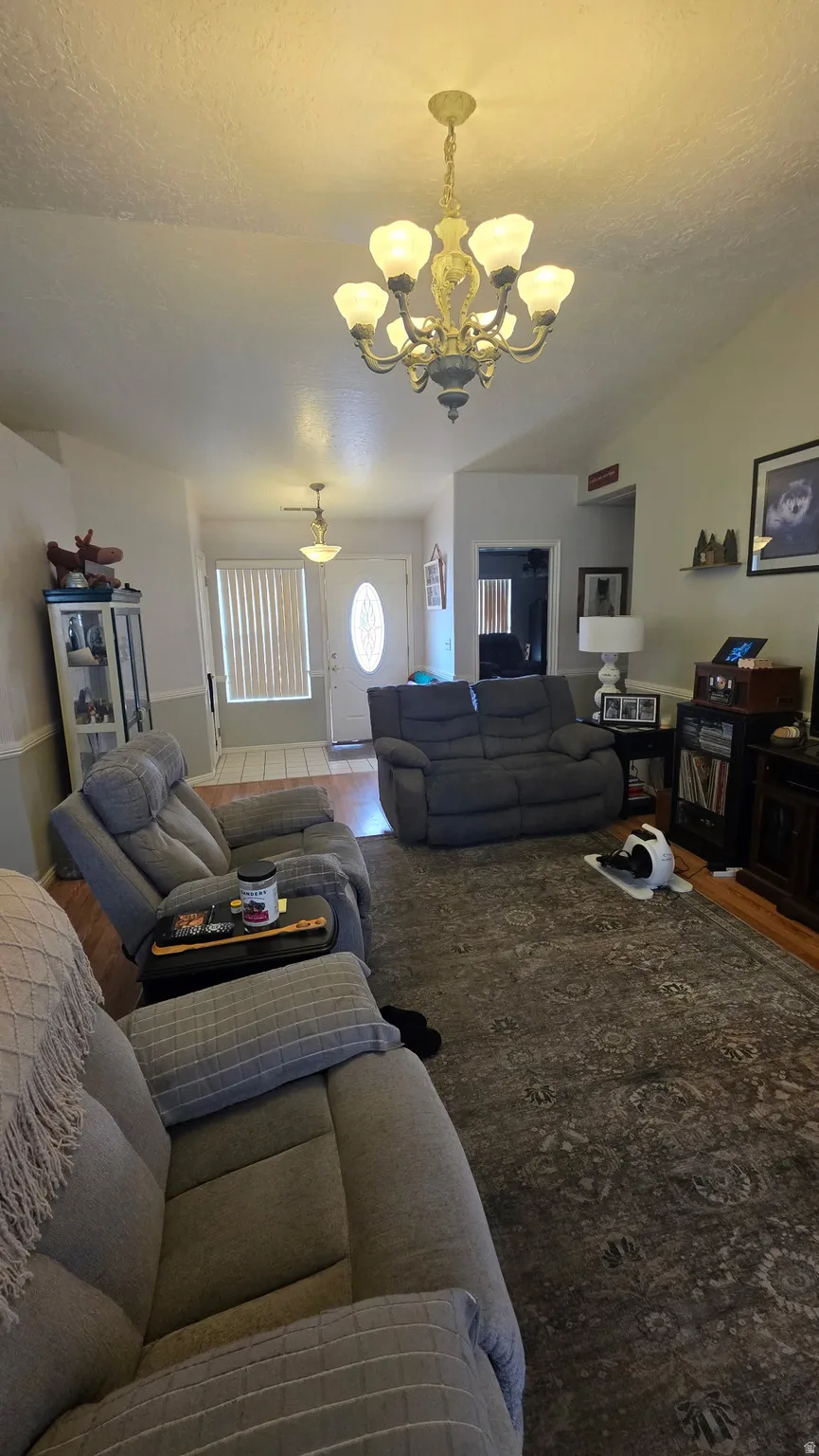 Vaulted ceiling with an ornate chandelier, white paneled door with an oval glass insert, and wood-finish flooring
