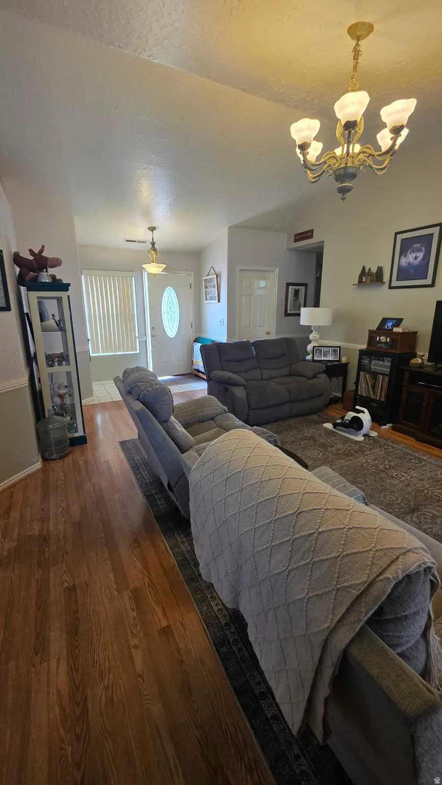 Vaulted ceilings with a brass chandelier, wood-finish flooring, and a white entry door with a decorative glass insert