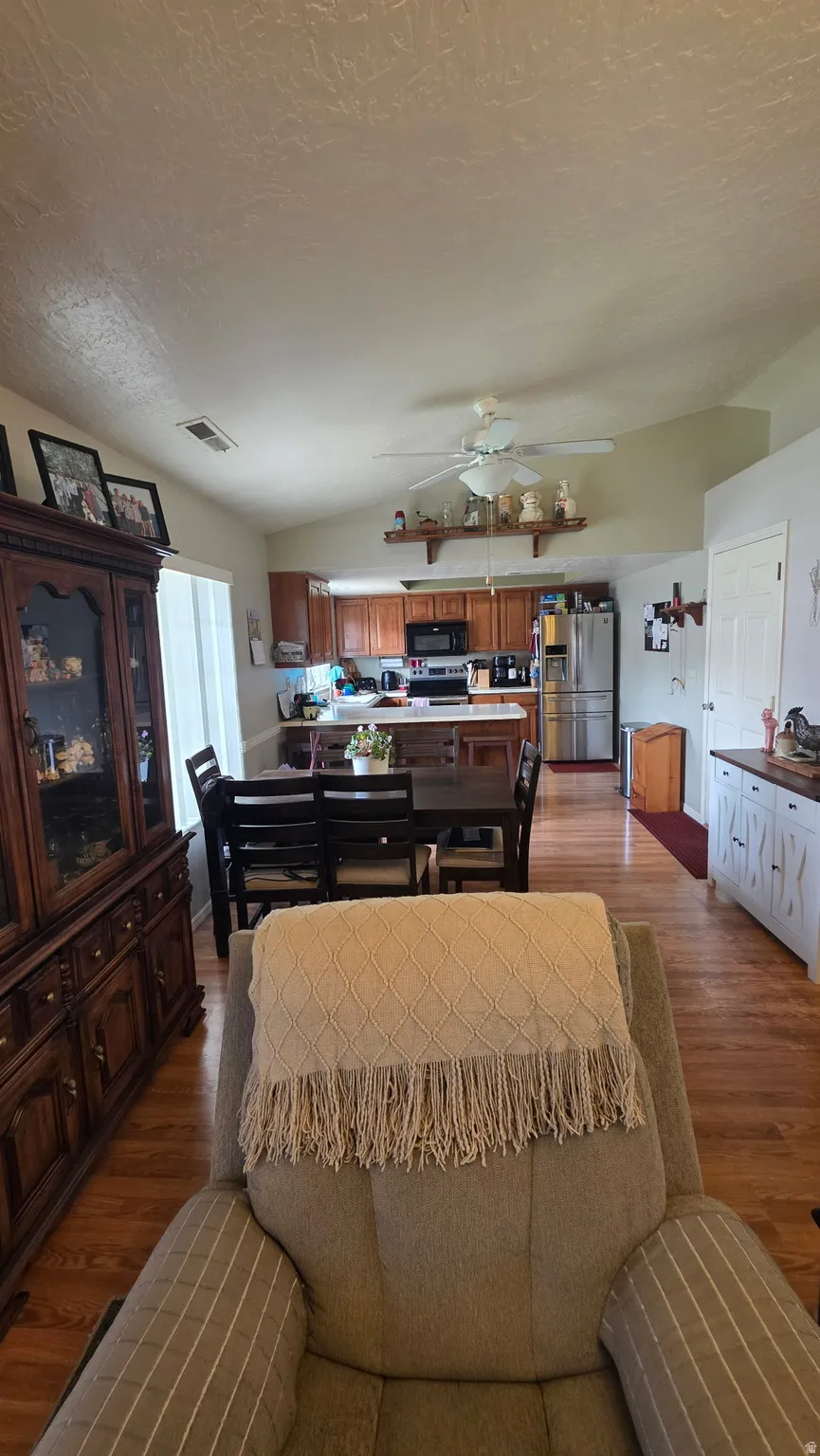 Vaulted ceiling with a ceiling fan, wood-finish flooring, kitchen with stainless steel appliances, and wood cabinetry