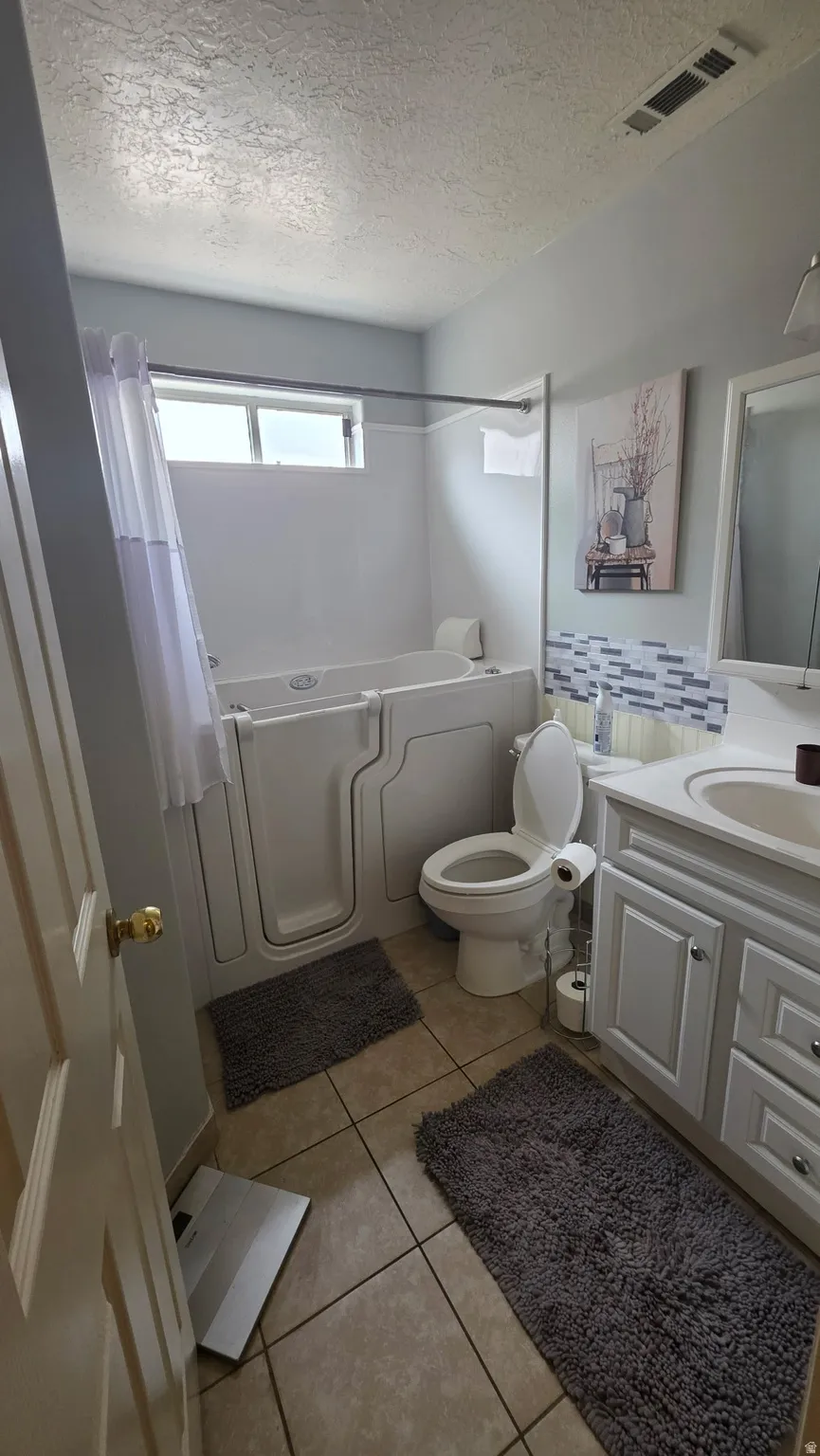 Bathroom featuring a walk-in tub, single vanity with white cabinetry, tile flooring, and a toilet
