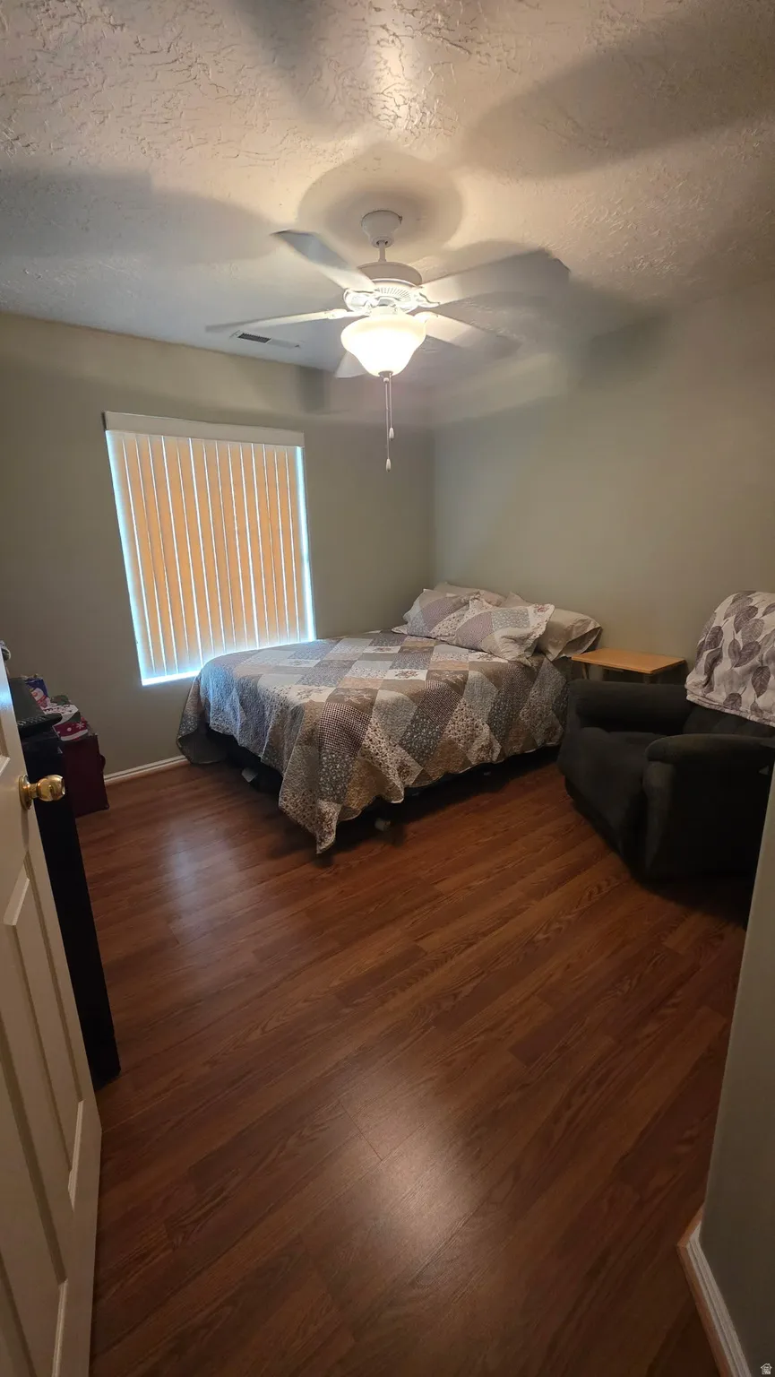 Wood-finish flooring, ceiling fan with integrated lighting, window with vertical blinds, and neutral wall tones