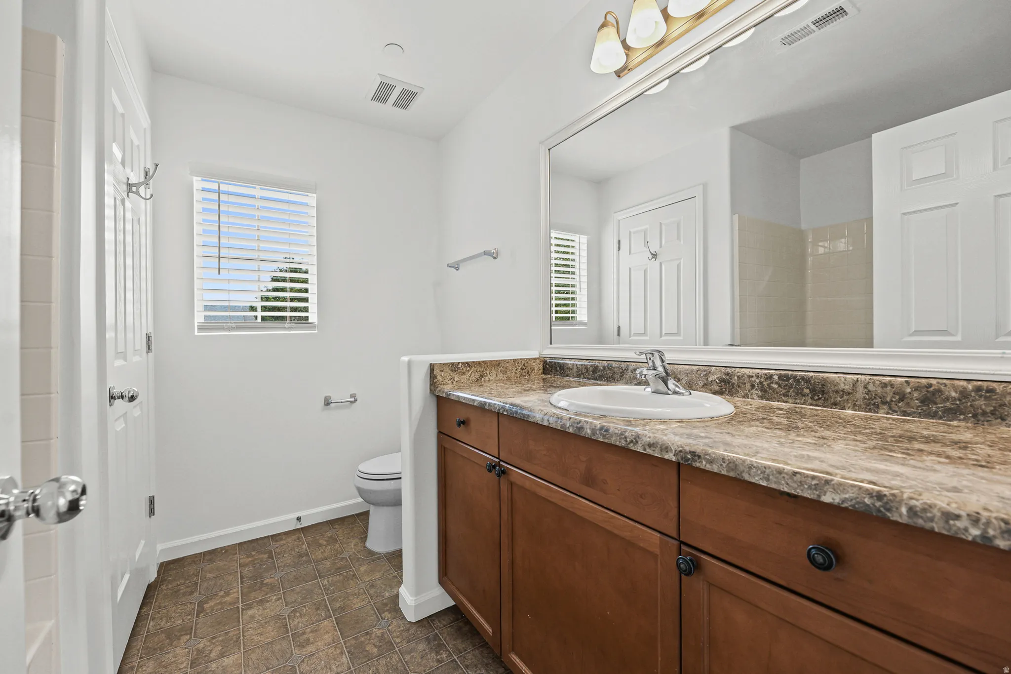 Bathroom featuring a vanity with a surface-mounted sink, a large mirror, rich wood-finish cabinetry, and tiled flooring