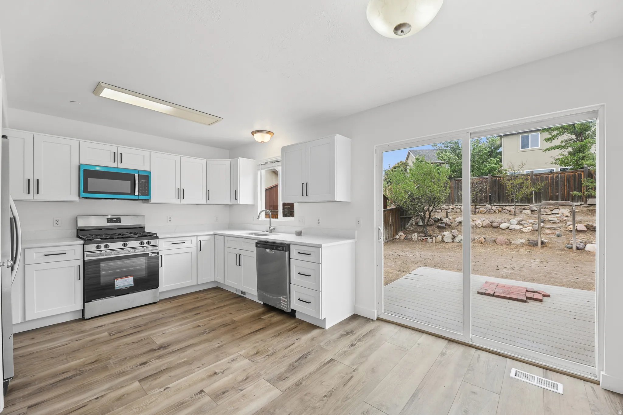 White cabinetry, stainless steel appliances, wood-finish flooring, white countertops, and sliding glass doors
