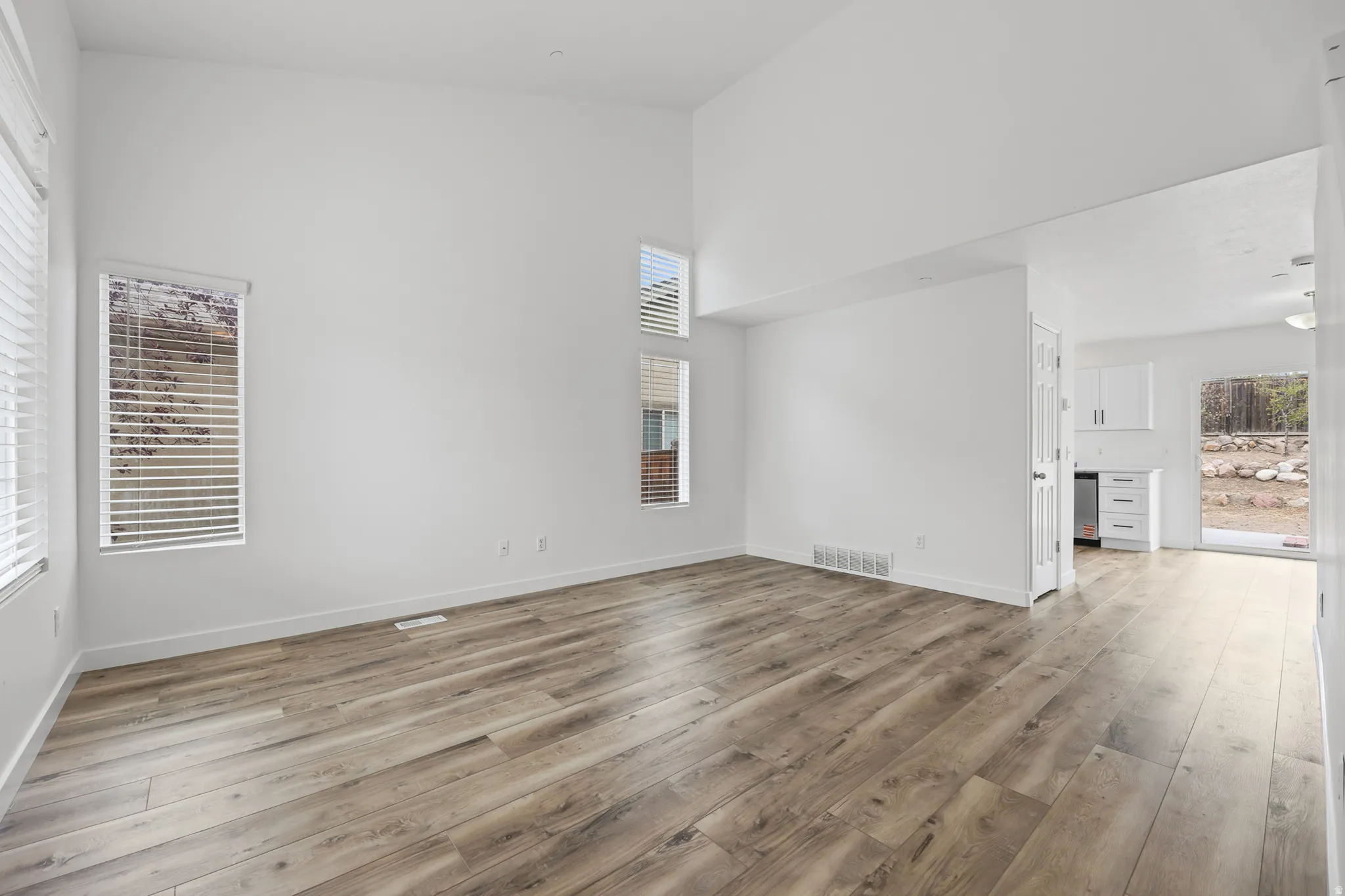 Vaulted ceilings, wood-finish flooring, multiple windows with blinds, white painted walls, and a white paneled door